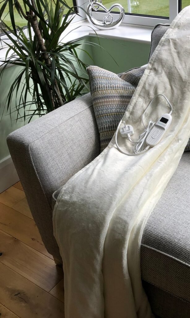 CoziPlus Classic heated throw in cream draped over a sofa