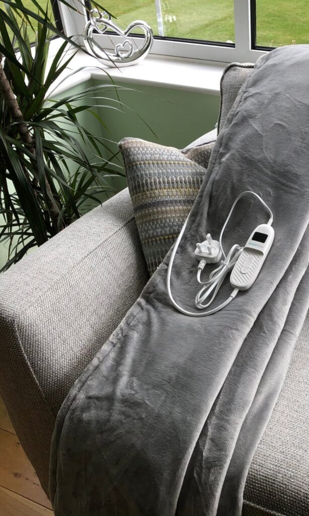 CoziPlus Classic heated throw in light grey draped over a sofa