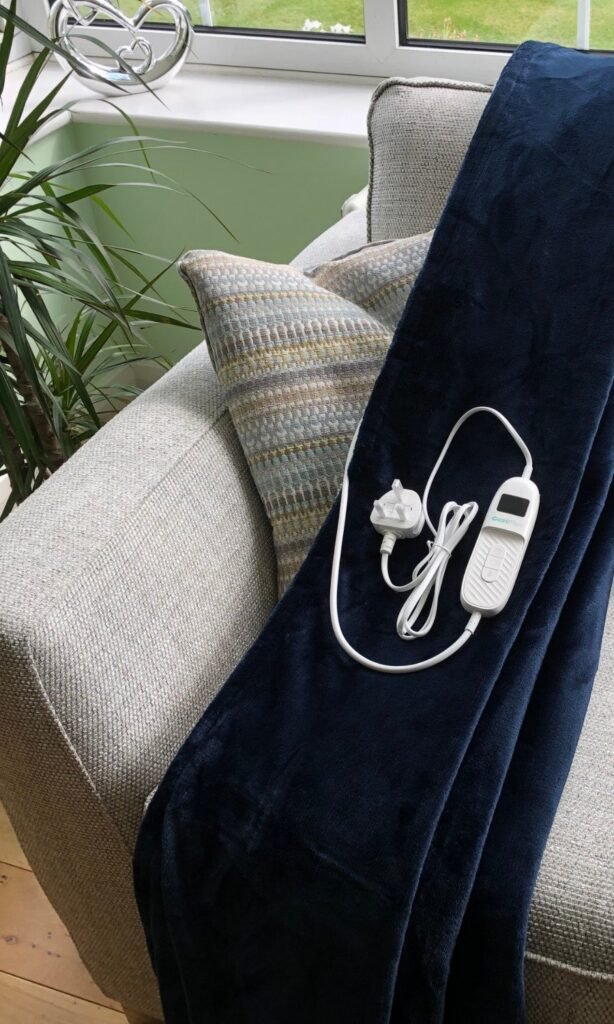 Navy CoziPlus heated throw draped over a grey sofa
